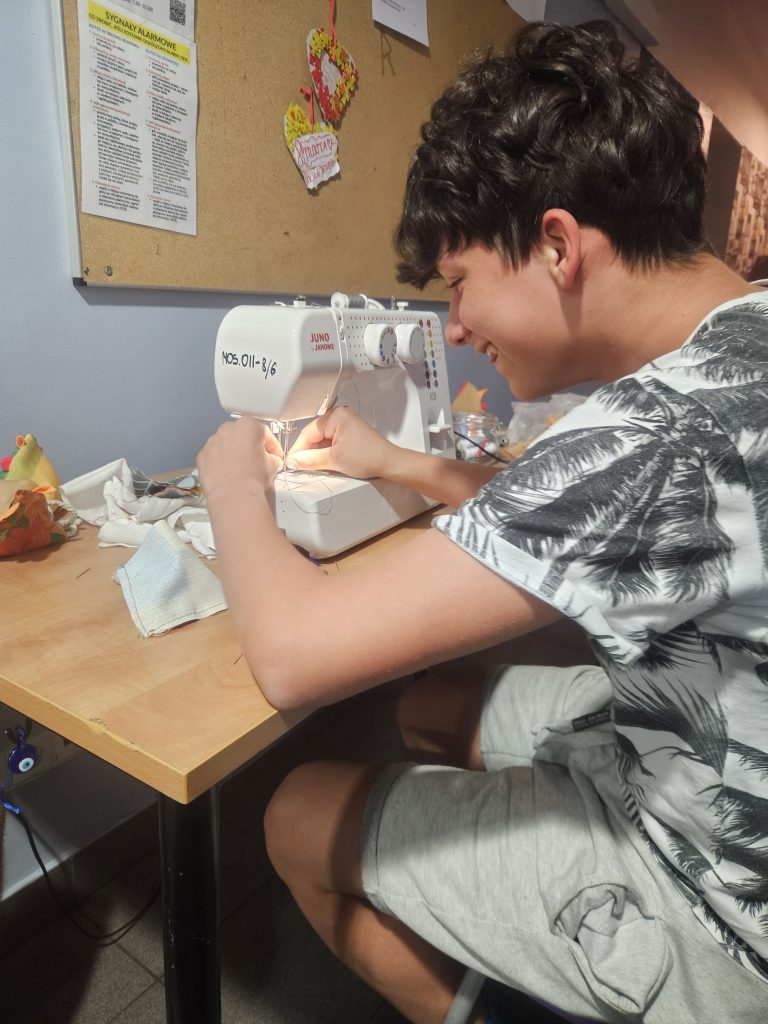 Uśmiechnięty wychowanek pracuje na maszynie do szycia