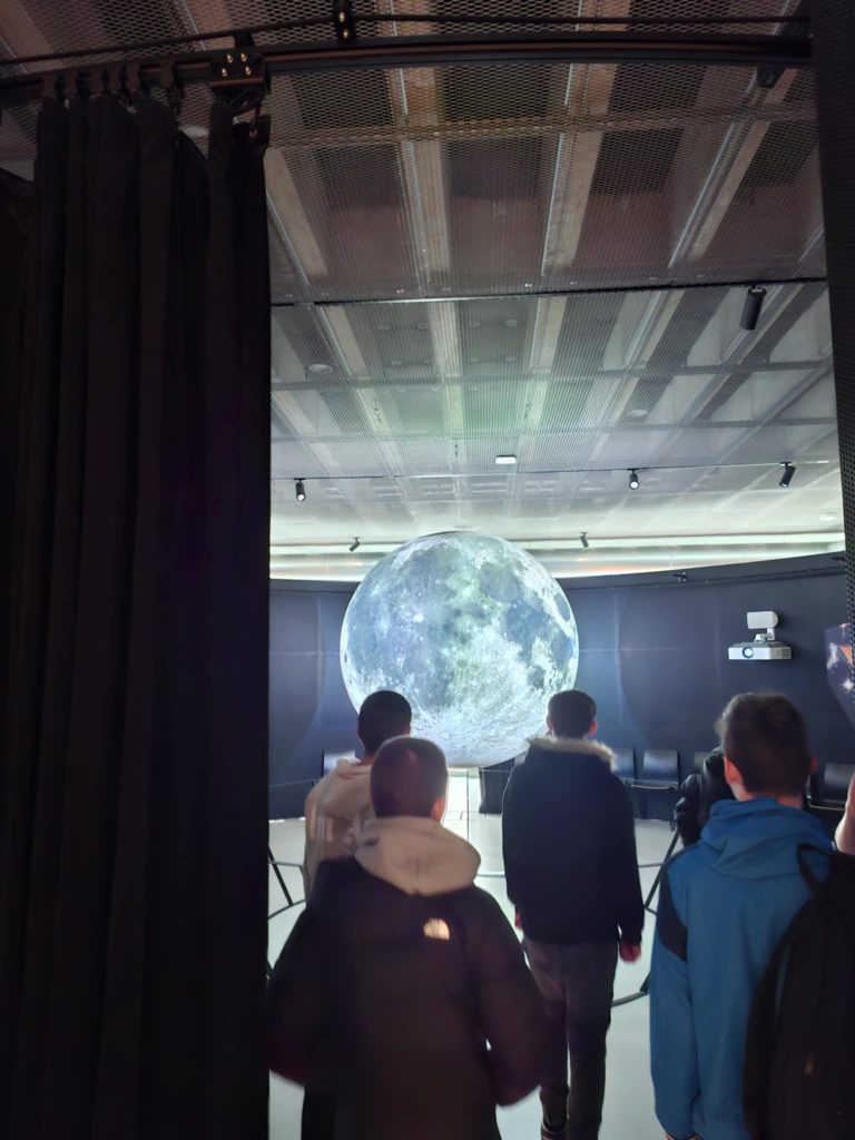 Chłopcy wchodzący na wystawę przedstawiającą holograficzny model księżyca